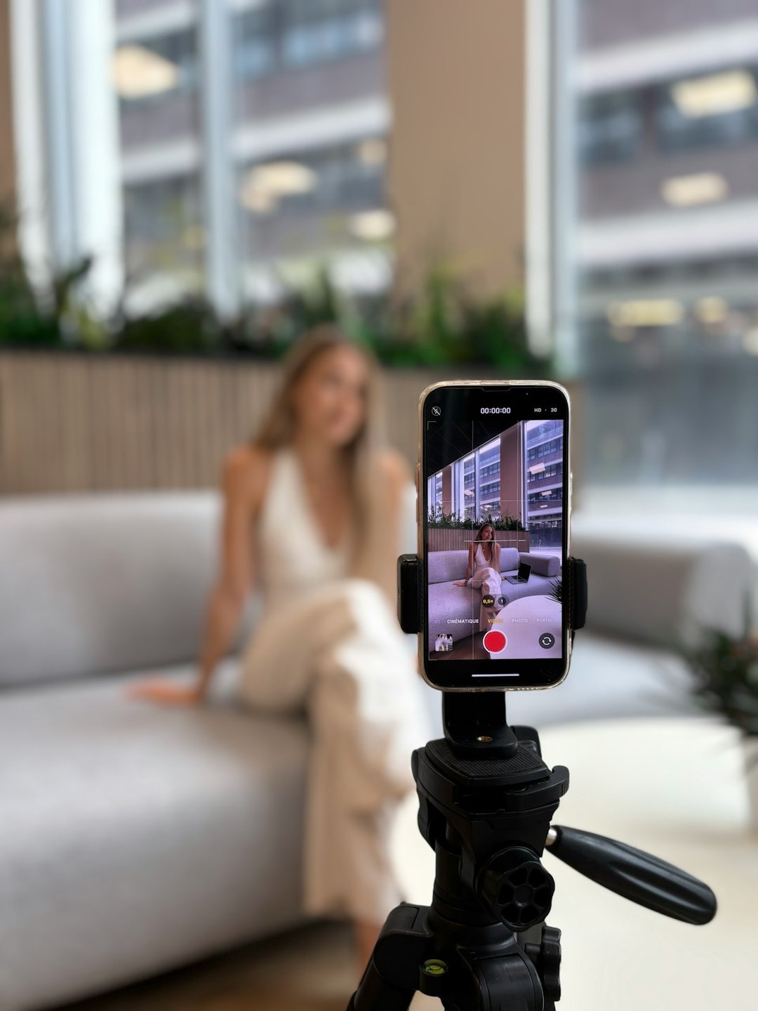 A smartphone mounted on a tripod filming a person creating video content indoors