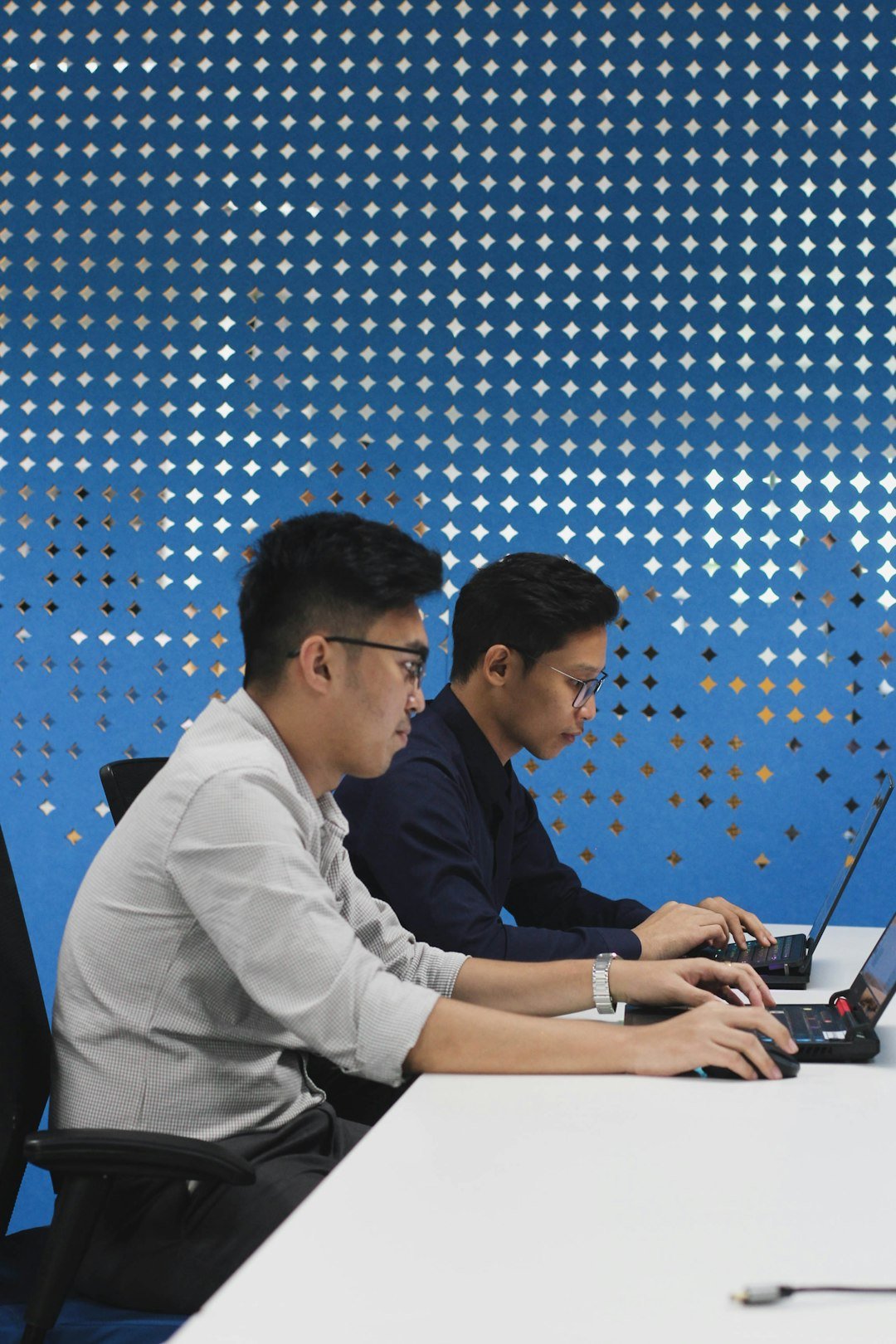 Two young developers working side by side on laptops in an office