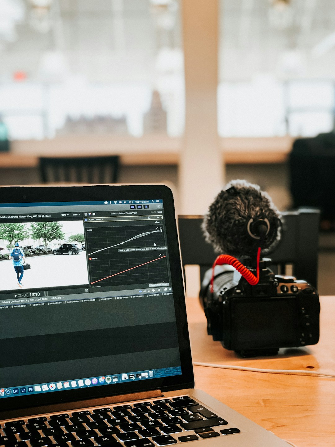 A laptop showing a video editing timeline beside a camera with a shotgun microphone