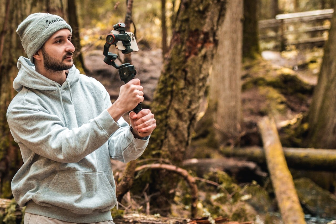 A creator films video on a smartphone mounted to a handheld gimbal outdoors