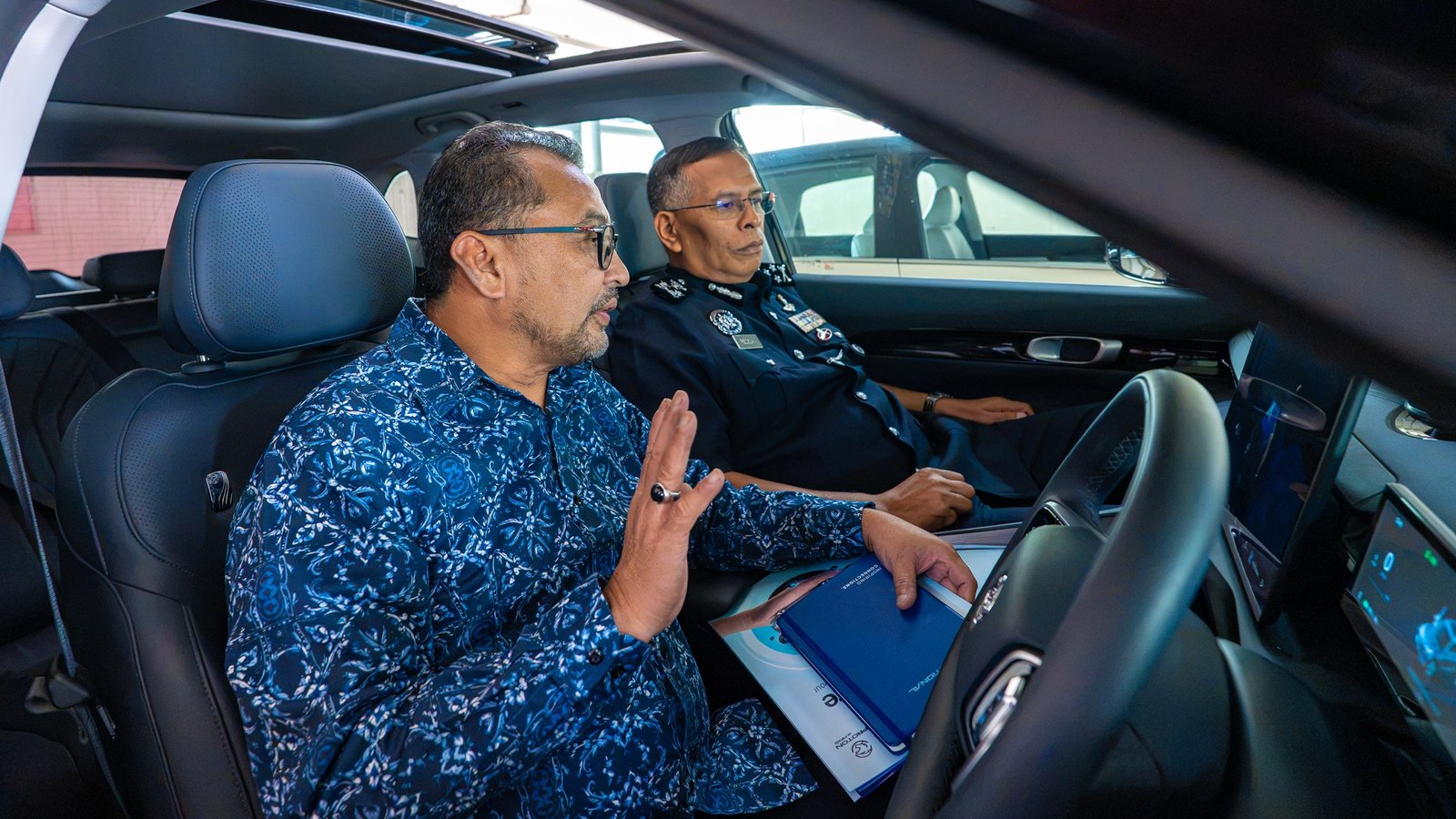 A PDRM officer examines the interior and dashboard of a Proton e.MAS during the evaluation handover