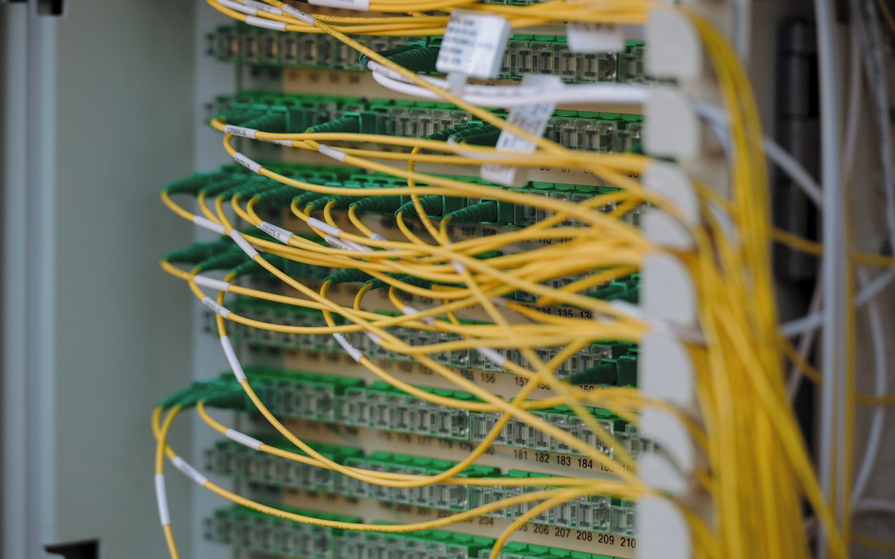 Yellow fibre optic patch cables running across a numbered network panel in a data centre