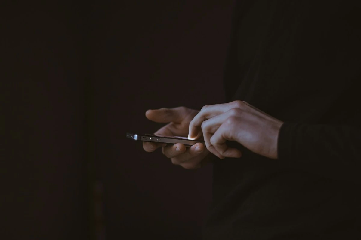 A person taps at a smartphone in low light, using a mobile app