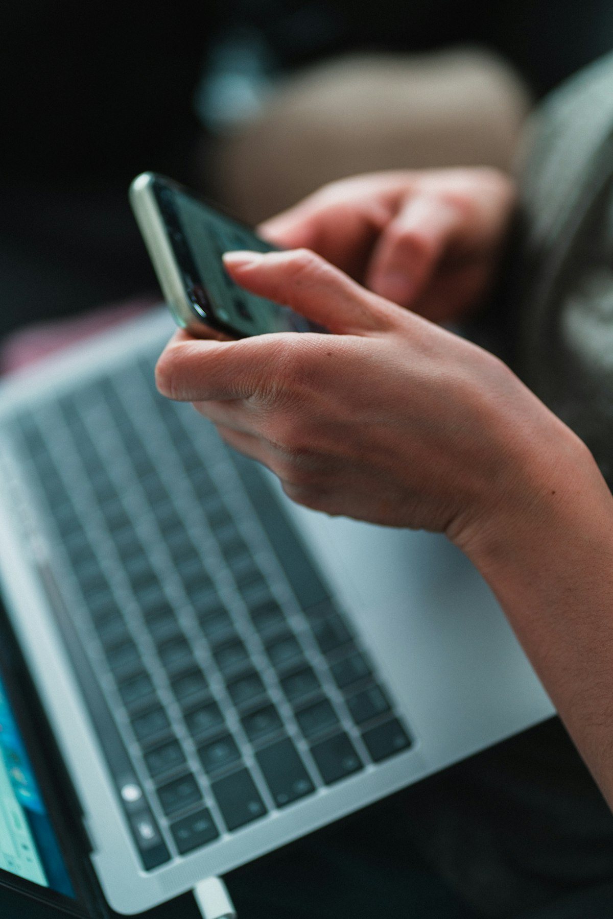A hand holds a smartphone over a laptop keyboard, the setting for most online scam transfers