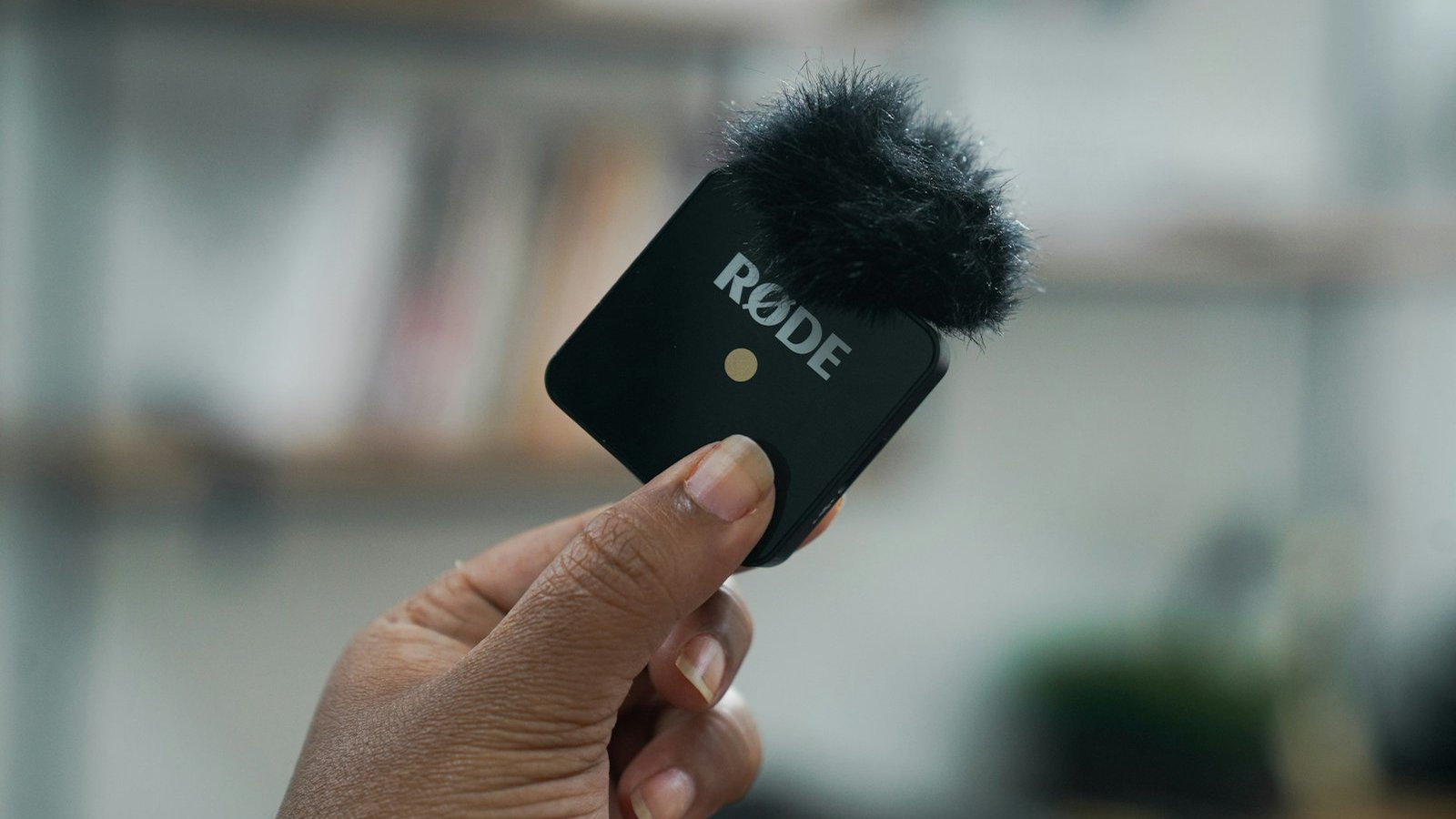 A hand holds a small wireless microphone used to record voice audio