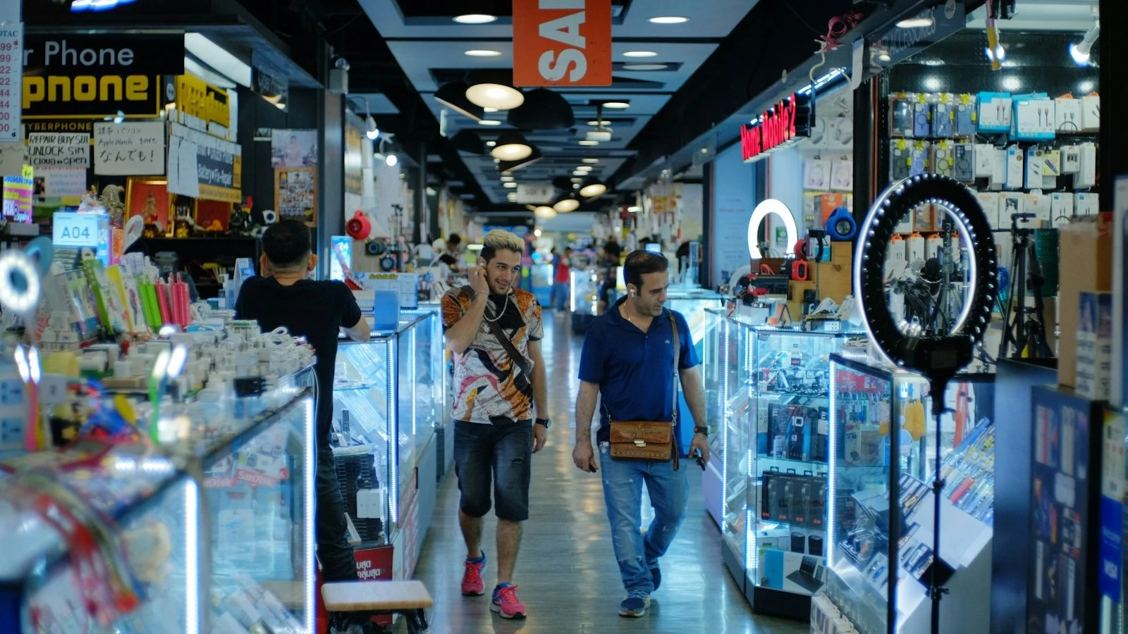 Shoppers walking through a busy electronics market lined with gadget stalls