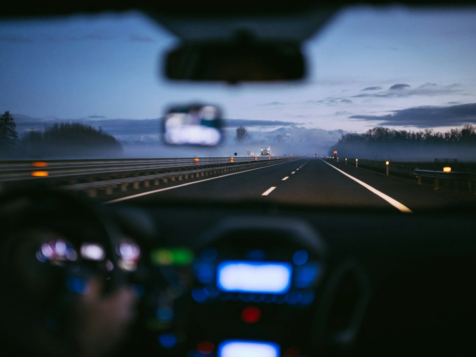 Pemandangan lebuh raya ketika senja dari dalam kereta yang bergerak, dengan papan pemuka bercahaya
