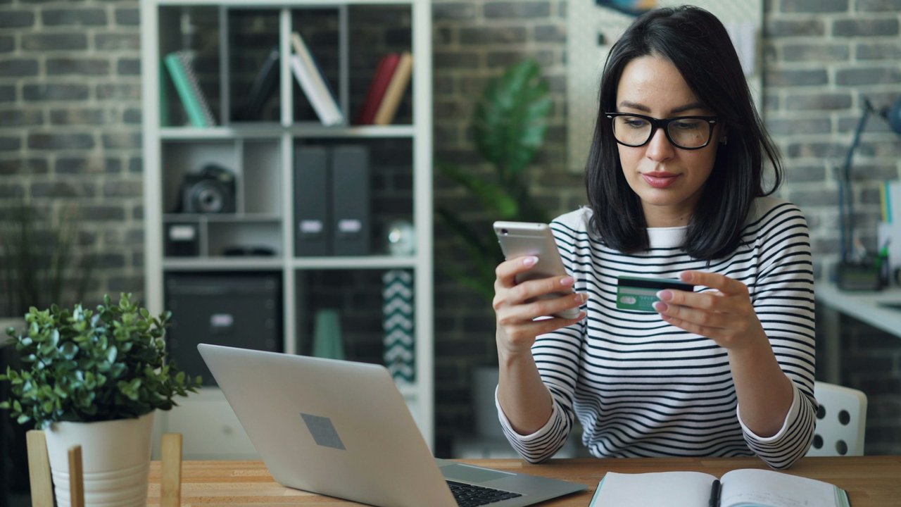 Woman making an online payment with a phone and a bank card