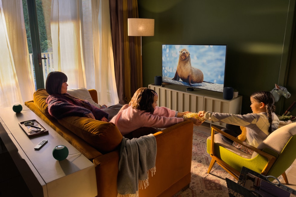 Sebuah keluarga menonton Apple TV 4K baharu dengan empat pembesar suara HomePod mini 2 hijau disusun untuk bunyi surround home theatre