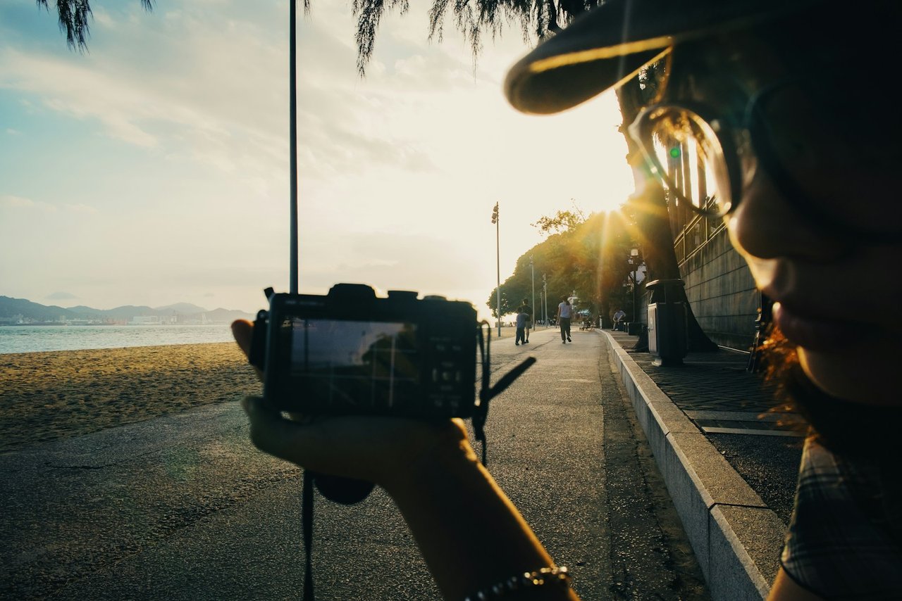 A content creator films a seaside sunset on a compact camera