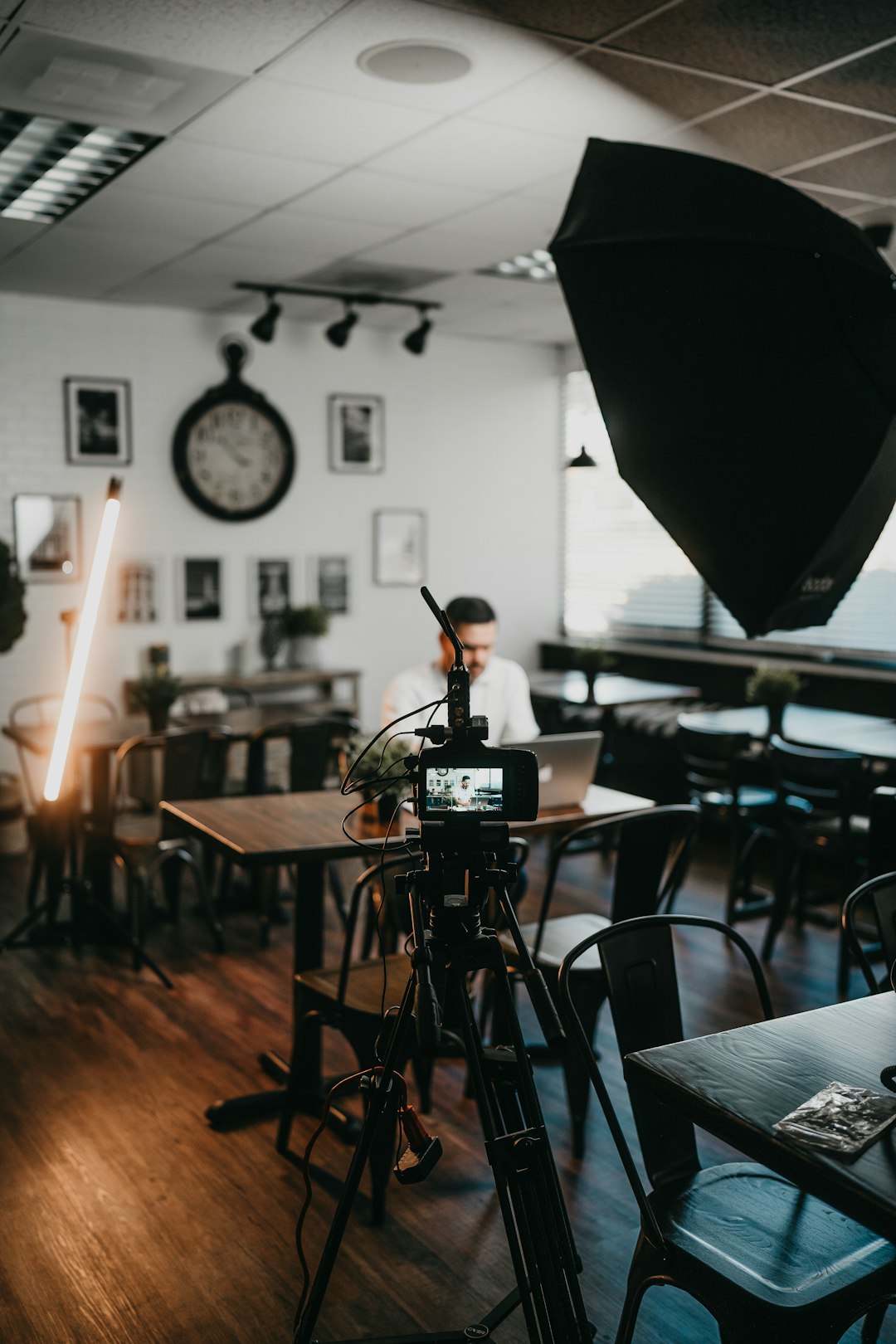 A camera on a tripod with studio lighting set up to film in a cafe