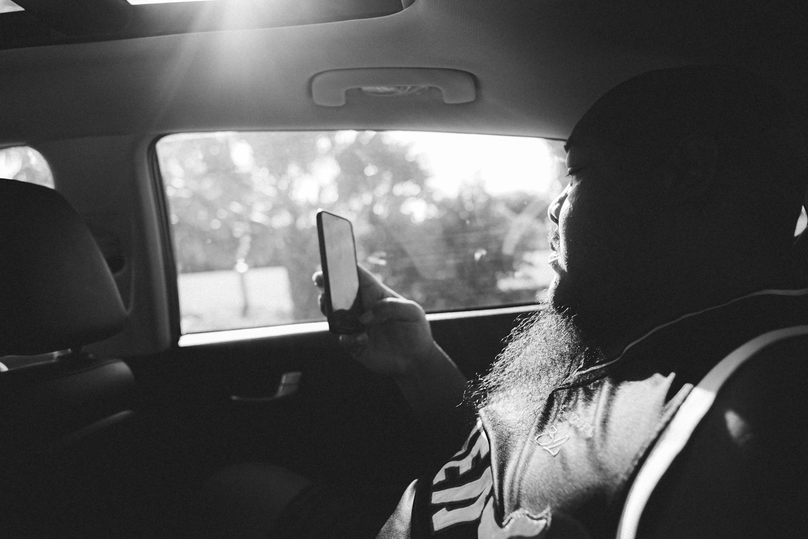 A passenger in the back seat of a car looks at a smartphone