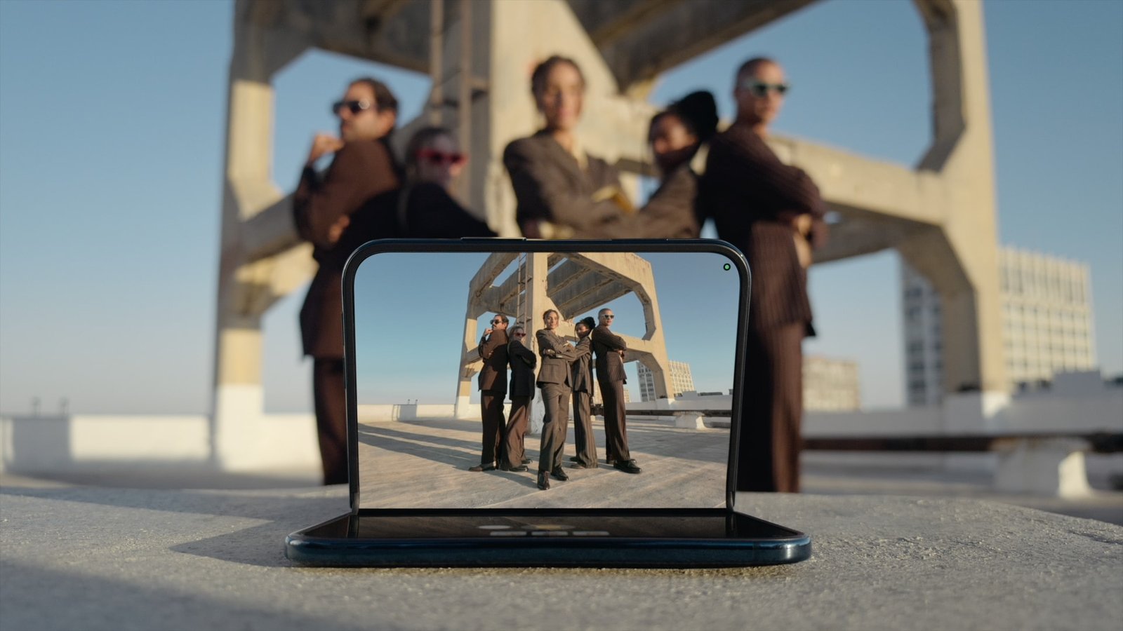 iPhone Duo propped open on a rooftop shooting a group photo with Duo Preview on the outer display, Apple press image