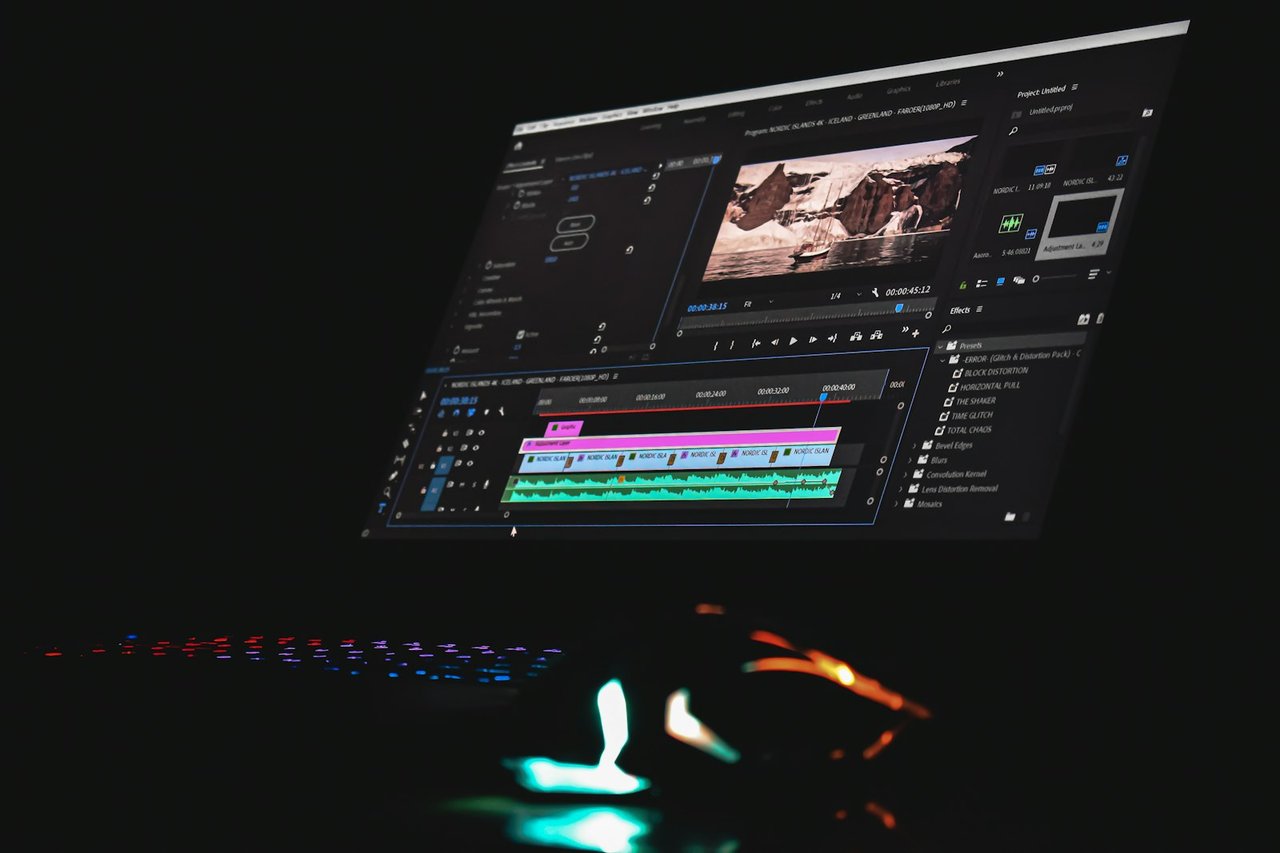 A video editing timeline open on a monitor above a backlit keyboard