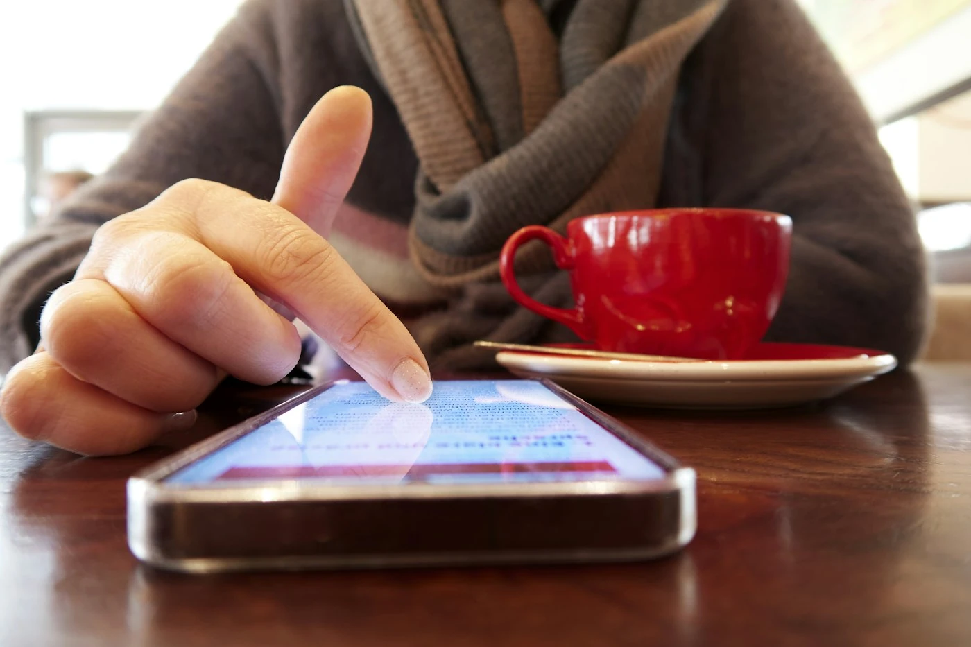 A person reading on a smartphone in a cafe with a red coffee cup
