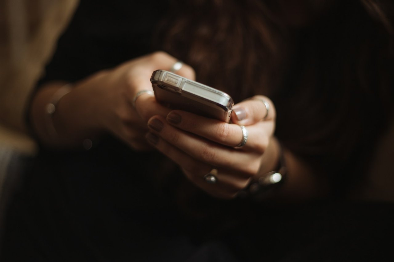 Seseorang memegang dan menggunakan telefon pintar dengan kedua-dua tangan