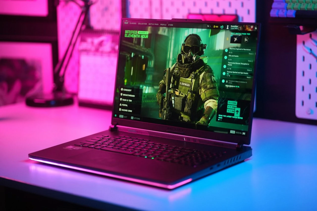 An ASUS ROG gaming laptop running a first-person shooter, lit by pink and blue RGB