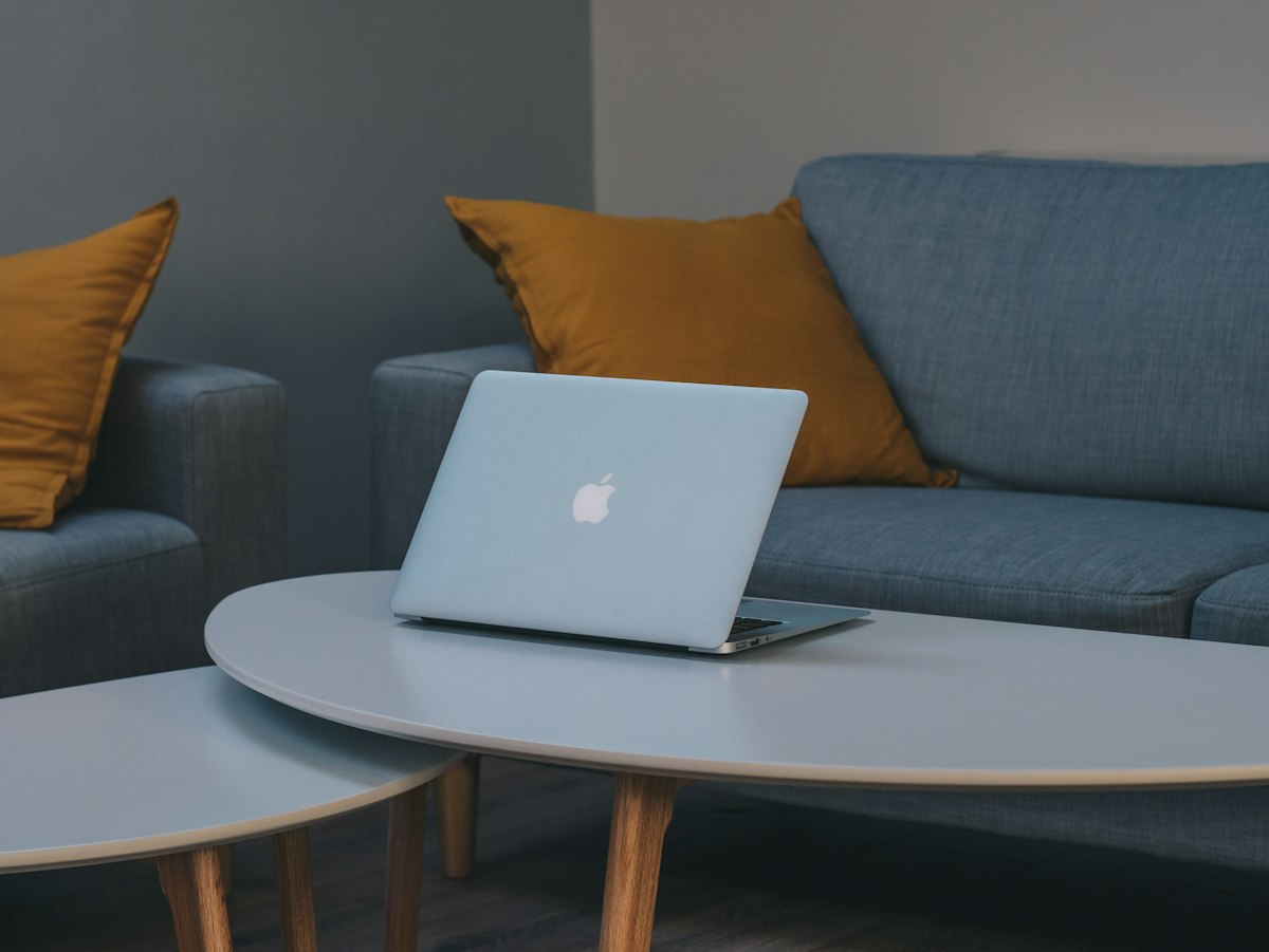 Sebuah MacBook terbuka di atas meja kopi di ruang tamu dengan sofa biru