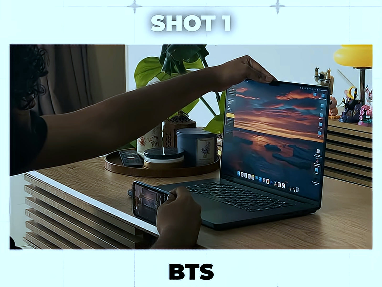 Reaching to prop up the phone recording rig beside a laptop, in the BTS half of Shot 1