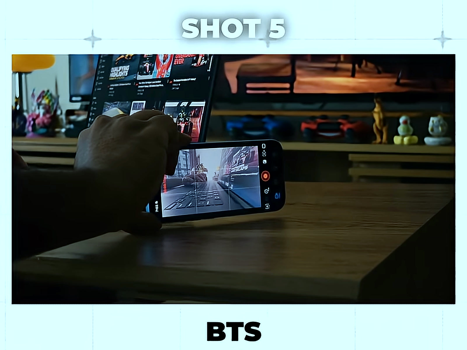 Holding the phone that is recording the next clip, with a motorsport broadcast playing on the screen behind it, in the BTS half of Shot 5