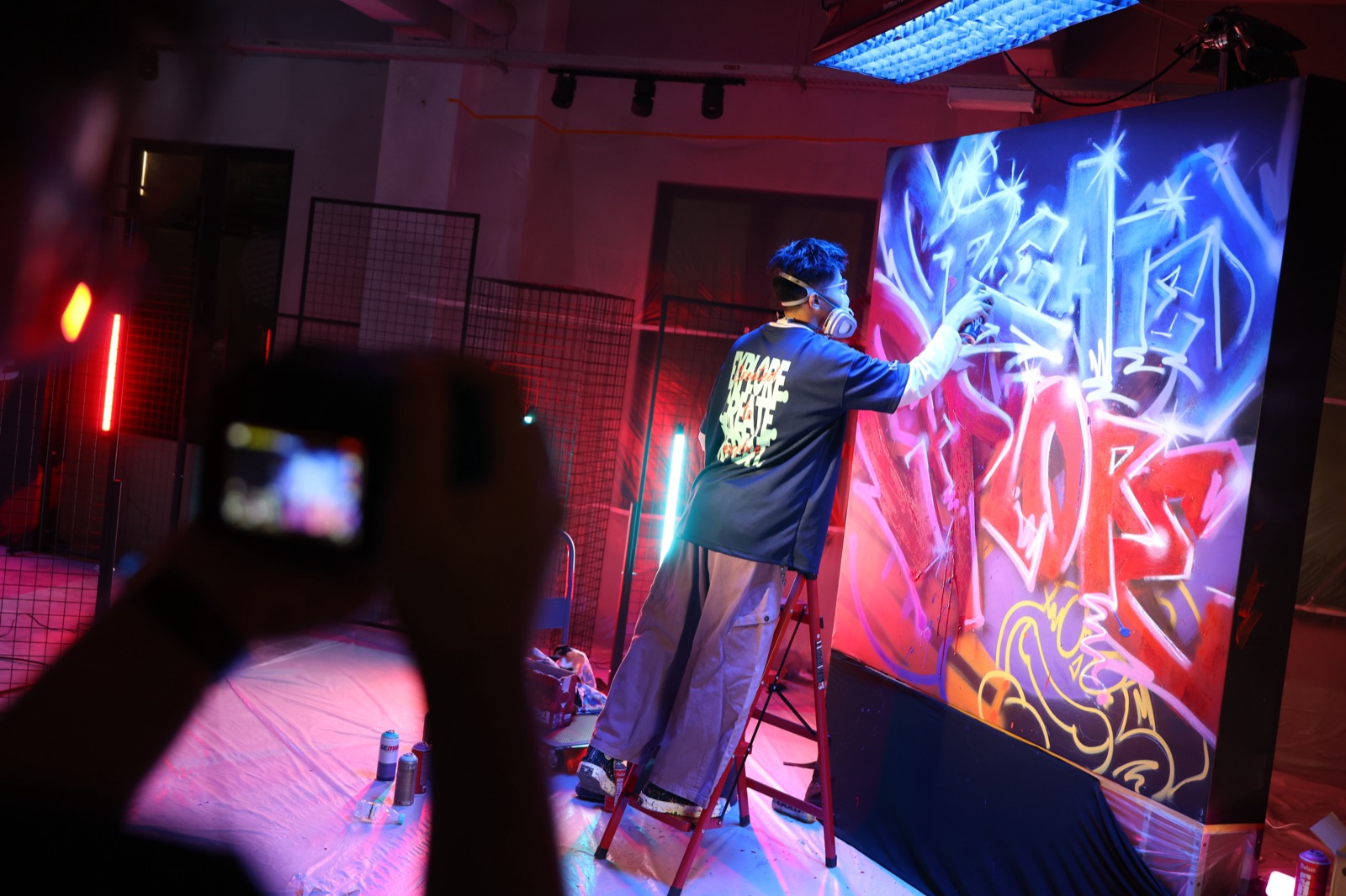 An attendee films a live graffiti artist painting the Created To Explore mural at the Kuala Lumpur tour stop